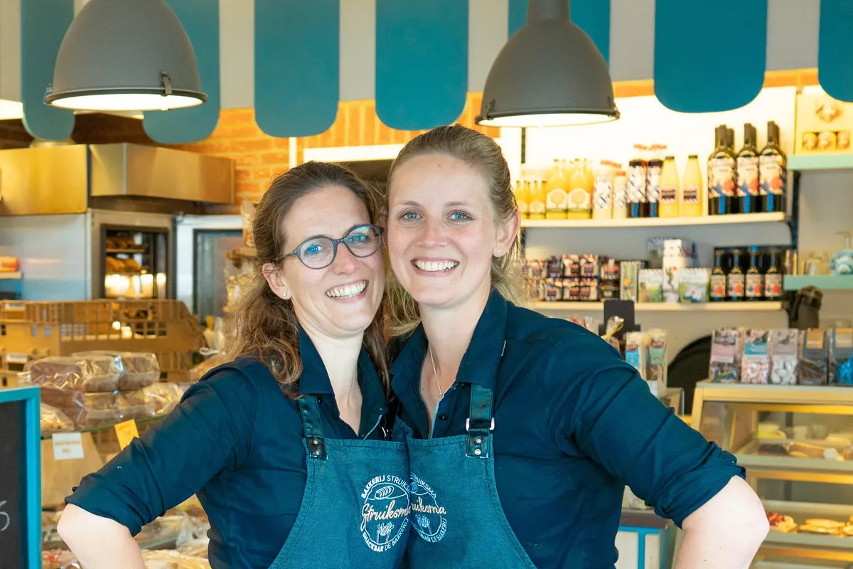 Twee lachende medewerkers in schorten met het Struiksma-logo, achter de toonbank in de winkel